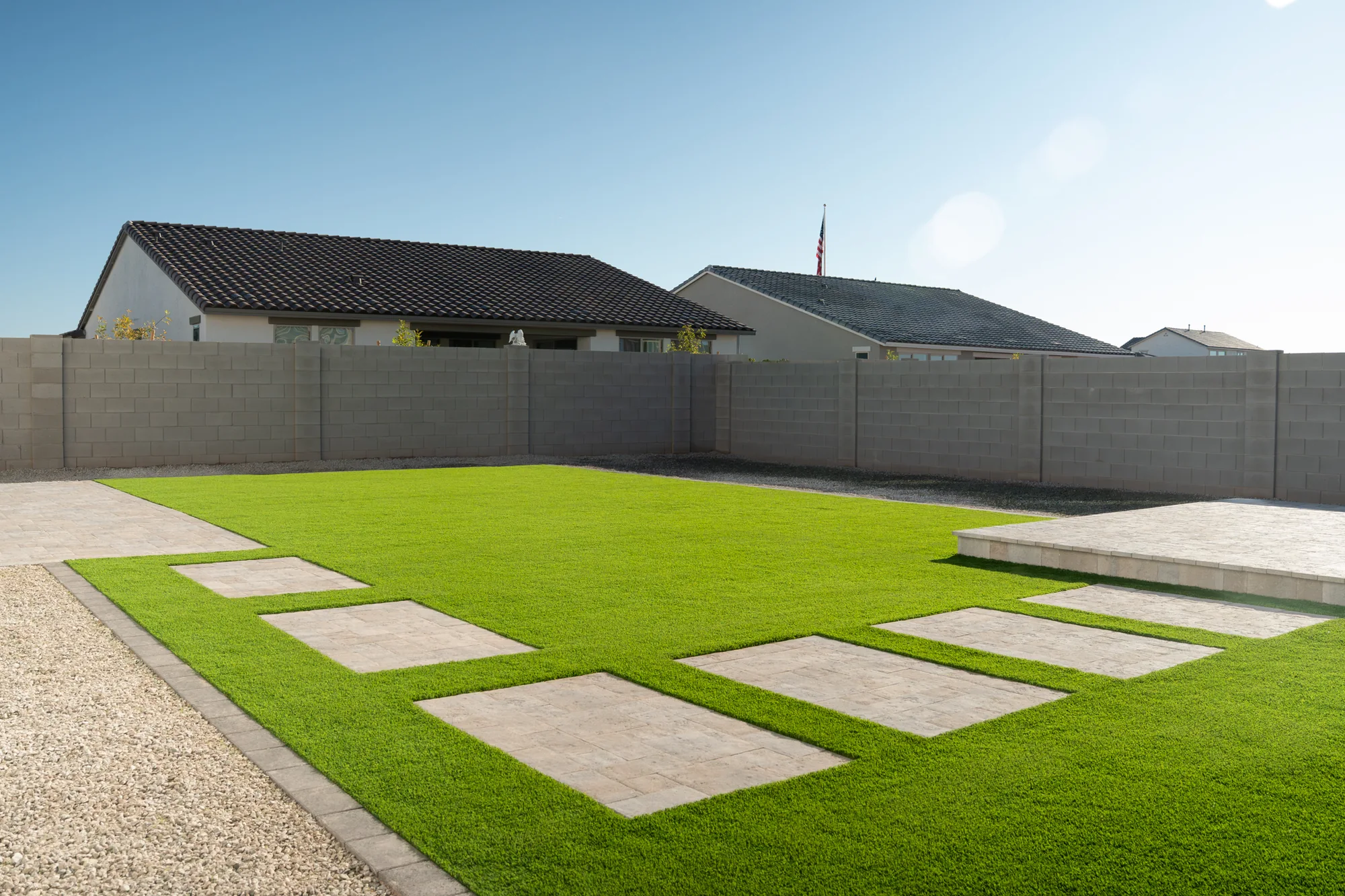 Artificial turf backyard with large paver stepping pads and a travertine patio