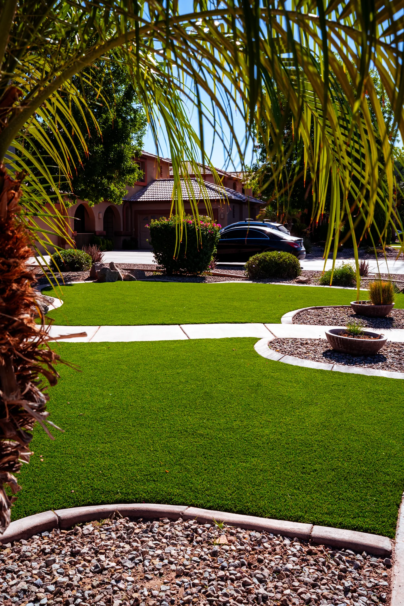 Artificial turf front lawn framed by palms, decorative gravel and a boulder