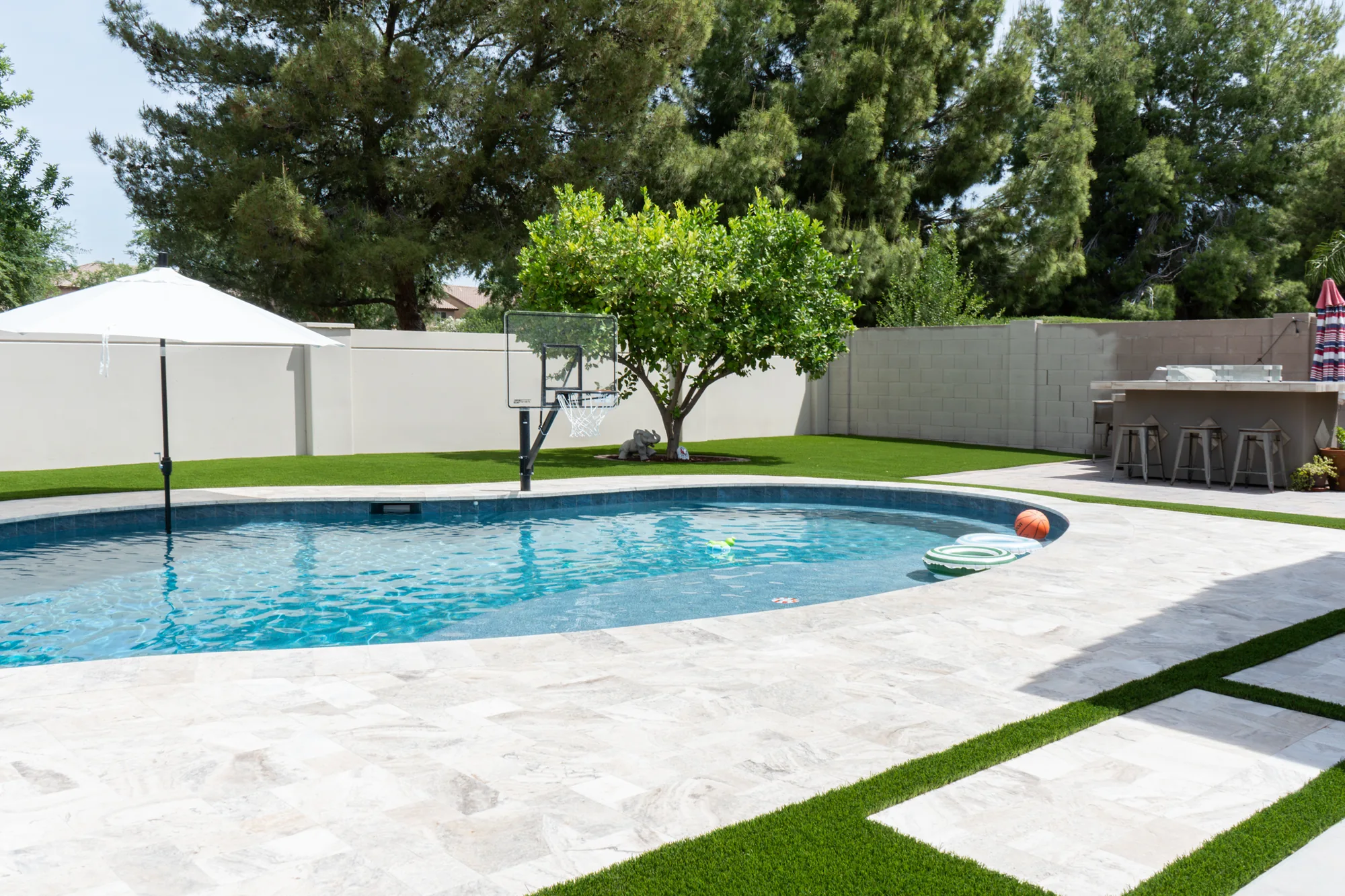 Poolside turf and stone paving with a backyard basketball hoop